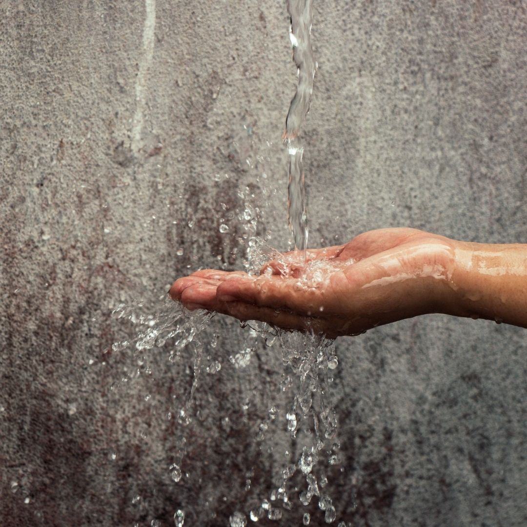 A hand reaching out to touch flowing water.